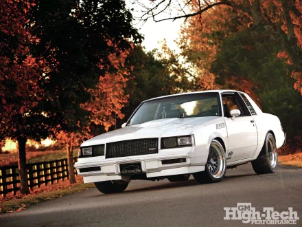 White Buick Riviera T‑Type on a country road framed by autumn foliage and a wooden fence; HD PC desktop wallpaper and background.