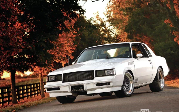 White Buick Riviera T‑Type on a country road framed by autumn foliage and a wooden fence; HD PC desktop wallpaper and background.