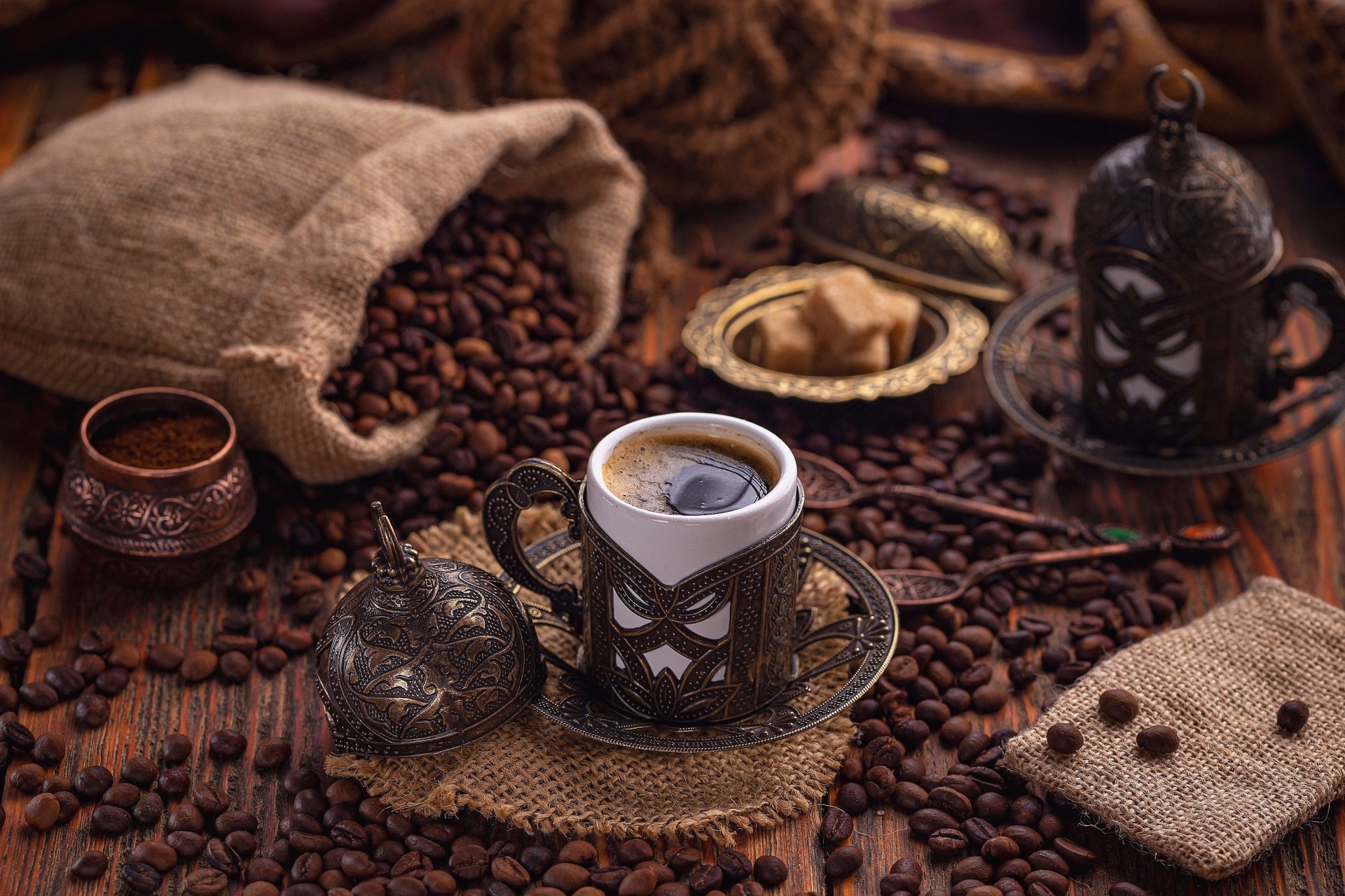 HD desktop wallpaper featuring a rustic coffee setup with a steaming cup in a decorative holder surrounded by scattered coffee beans and vintage accessories.