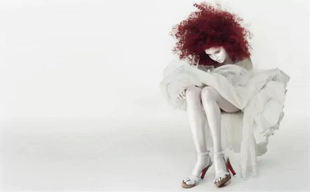 HD PC desktop wallpaper featuring celebrity Lily Cole seated, with striking red curly hair and a flowing white dress against a minimalist white background.