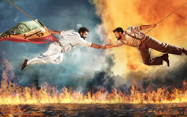 4K Ultra HD PC desktop wallpaper from the movie RRR: two heroic figures suspended midair over roaring flames, reaching to clasp hands against a stormy, smoky sky with flags.