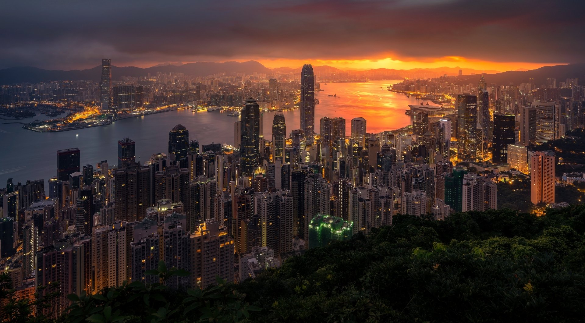 5K Ultra HD PC desktop wallpaper: Hong Kong skyline at sunset, harbor aglow and dense, man-made skyscrapers rising beneath dramatic clouds.