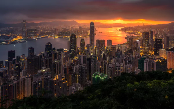 5K Ultra HD PC desktop wallpaper: Hong Kong skyline at sunset, harbor aglow and dense, man-made skyscrapers rising beneath dramatic clouds.