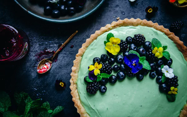 A vibrant food-themed 4K Ultra HD desktop wallpaper featuring a green cake topped with fresh blackberries, blueberries, and colorful edible flowers.