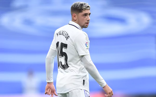 Federico Valverde in white Real Madrid jersey, on a pristine pitch under stadium lights, displaying skill and determination.