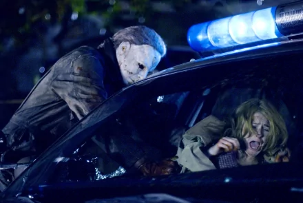 HD PC desktop wallpaper featuring a tense scene from the 2007 movie Halloween, showing Michael Myers attacking a woman near a police car with flashing lights.