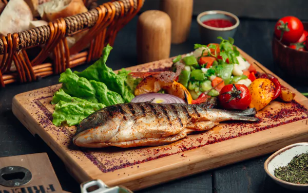 5K Ultra HD PC desktop wallpaper: food — a grilled whole fish on a wooden board with lettuce, roasted tomatoes, mixed salad, bread basket and seasoning.