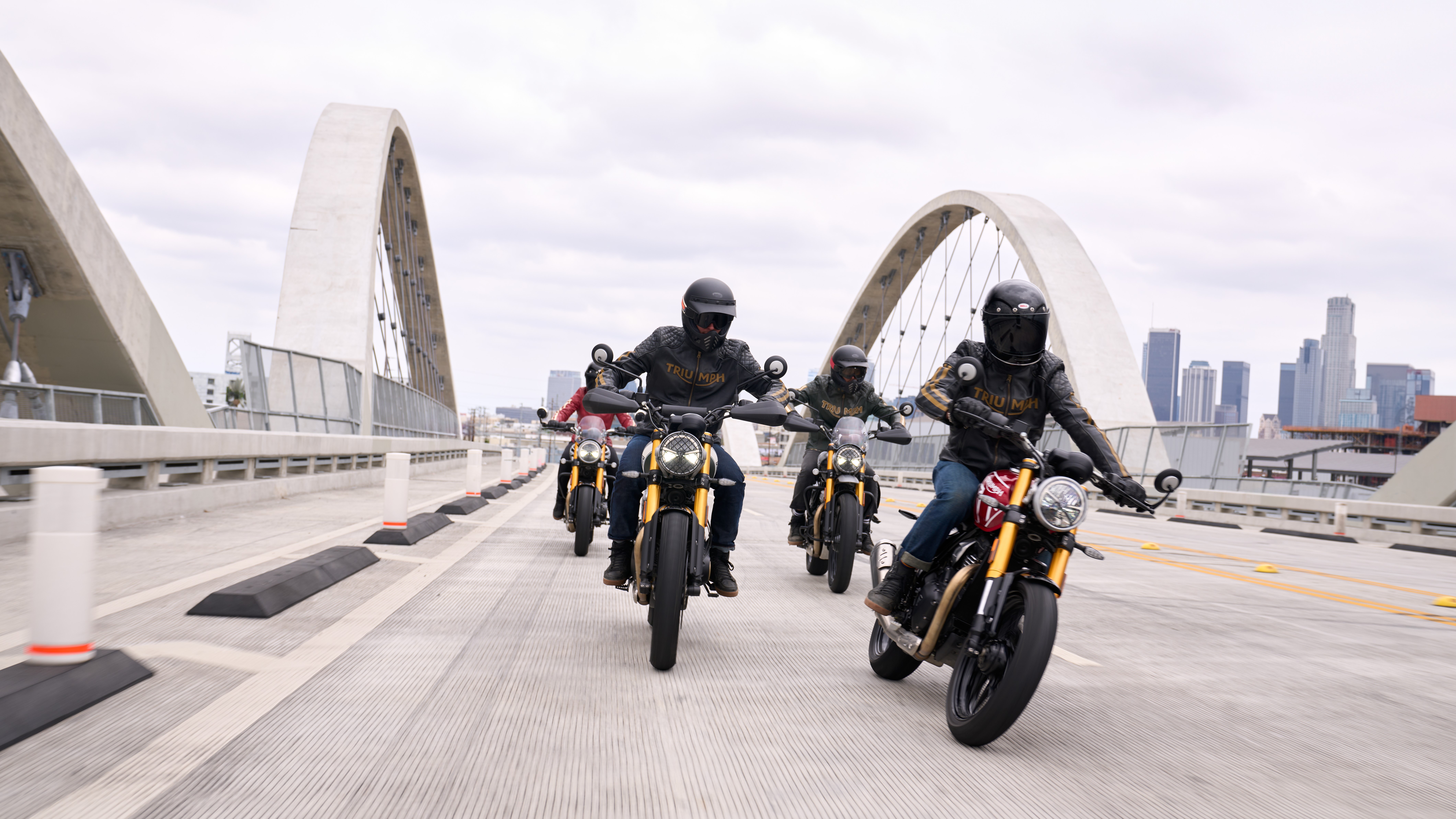 Triumph Speed 400 and Triumph Scrambler 400 X motorcycles riding on a bridge with city skyline in the background - HD Desktop Wallpaper