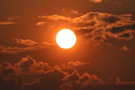 4K Ultra HD photography of a vibrant sunset with the sun glowing brightly amidst scattered clouds, captured as a stunning PC desktop wallpaper background.