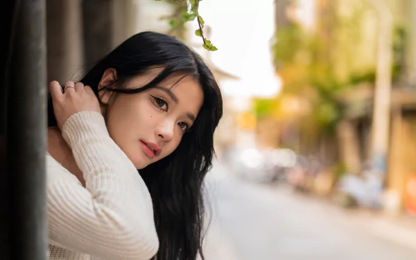 HD desktop wallpaper of an Asian woman with long black hair, wearing a cream sweater, posing outdoors with a blurred urban background.