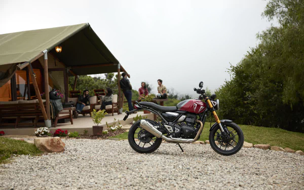 HD wallpaper of a Triumph Speed Twin 400 motorcycle parked in front of a cozy tent with people in the background.