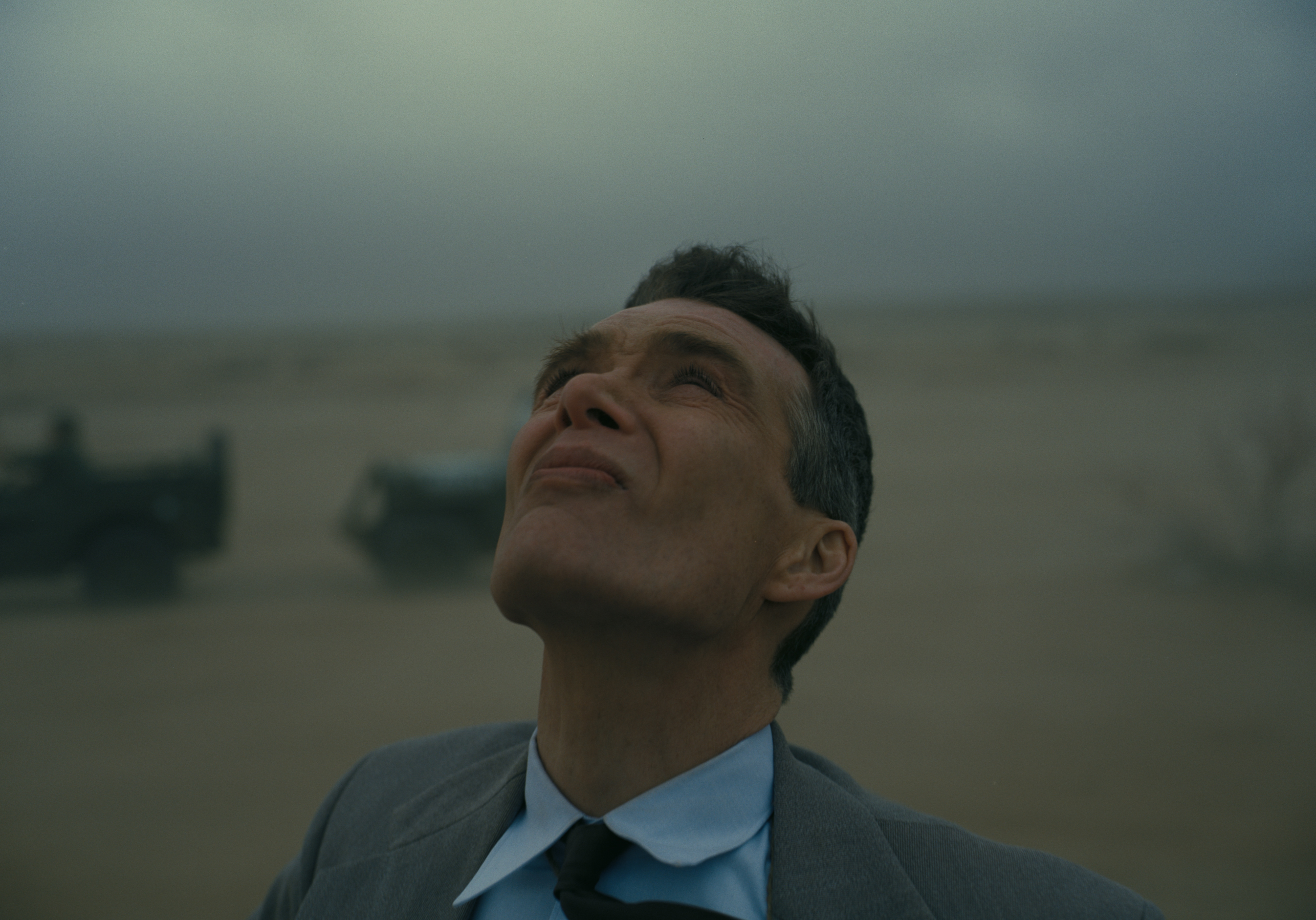 HD desktop wallpaper featuring a thoughtful man in a suit looking skyward with a desolate landscape in the background, reminiscent of Oppenheimer, evoking a contemplative mood.
