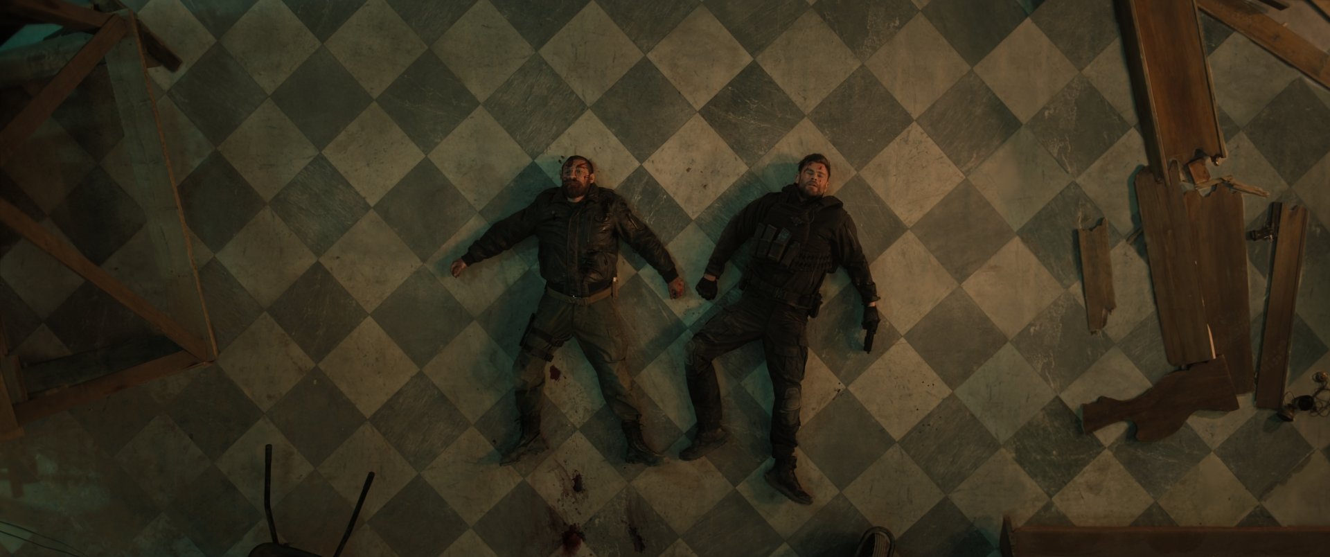 Overhead view of two male characters lying on a checkered floor in a scene from Extraction 2, featuring a high-definition desktop wallpaper aesthetic.
