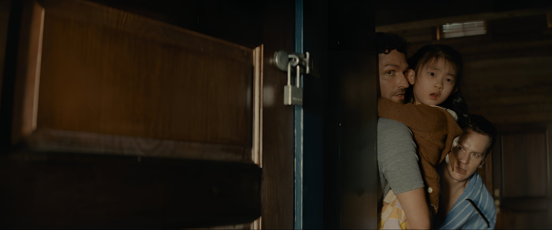 HD Desktop wallpaper featuring a suspenseful scene from Knock at the Cabin, with an adult and child peering through a partially opened door.