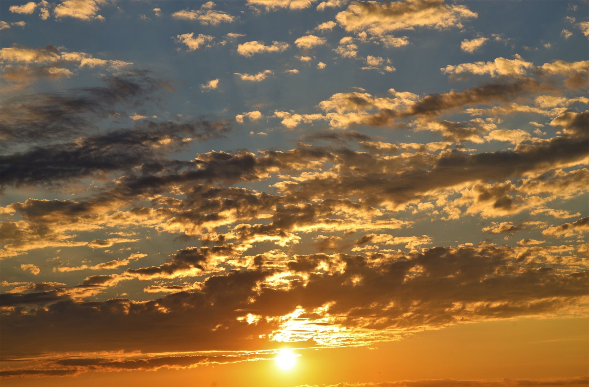 4K Ultra HD photography of a vibrant sunset with golden clouds scattered across the sky, creating a warm and serene atmosphere for a PC desktop background.