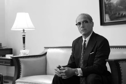 Black and white HD desktop wallpaper featuring a man portraying Oppenheimer in a contemplative pose, sitting in a classic office setting.