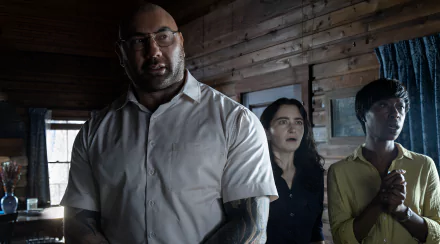 HD wallpaper featuring a scene from Knock at the Cabin with three tense characters indoors, expressing concern and anticipation.