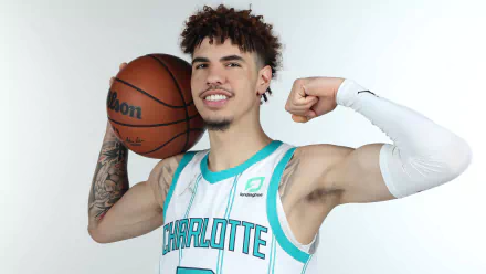 LaMelo Ball poses confidently in a Charlotte Hornets jersey, holding a basketball and flexing his arm. This HD desktop wallpaper captures the dynamic spirit of sports.