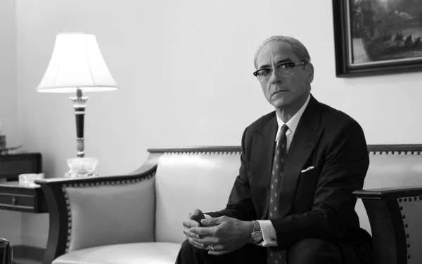 Black and white HD desktop wallpaper featuring a man portraying Oppenheimer in a contemplative pose, sitting in a classic office setting.