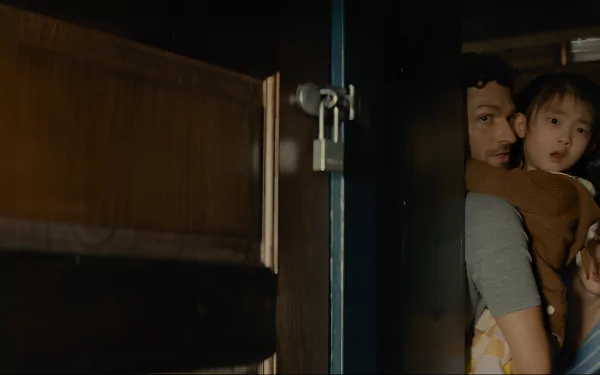 HD Desktop wallpaper featuring a suspenseful scene from Knock at the Cabin, with an adult and child peering through a partially opened door.