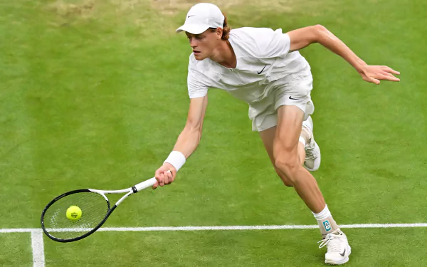 Jannik Sinner stretches during a match at Wimbledon 2023, showcasing his athleticism on the grass court in this dynamic tennis sports wallpaper.