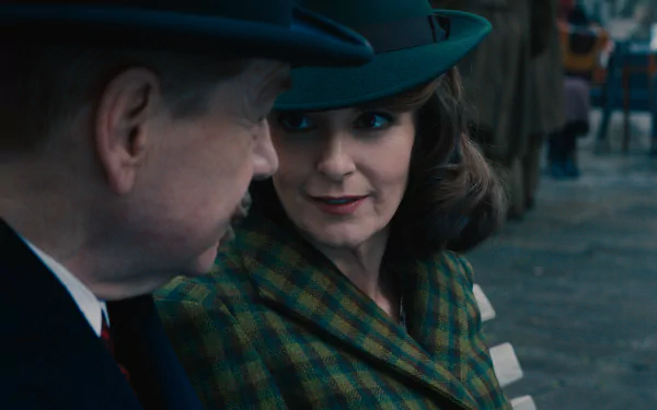 HD wallpaper featuring a scene from 'A Haunting in Venice' with a woman in a hat and plaid coat engaging in a conversation.