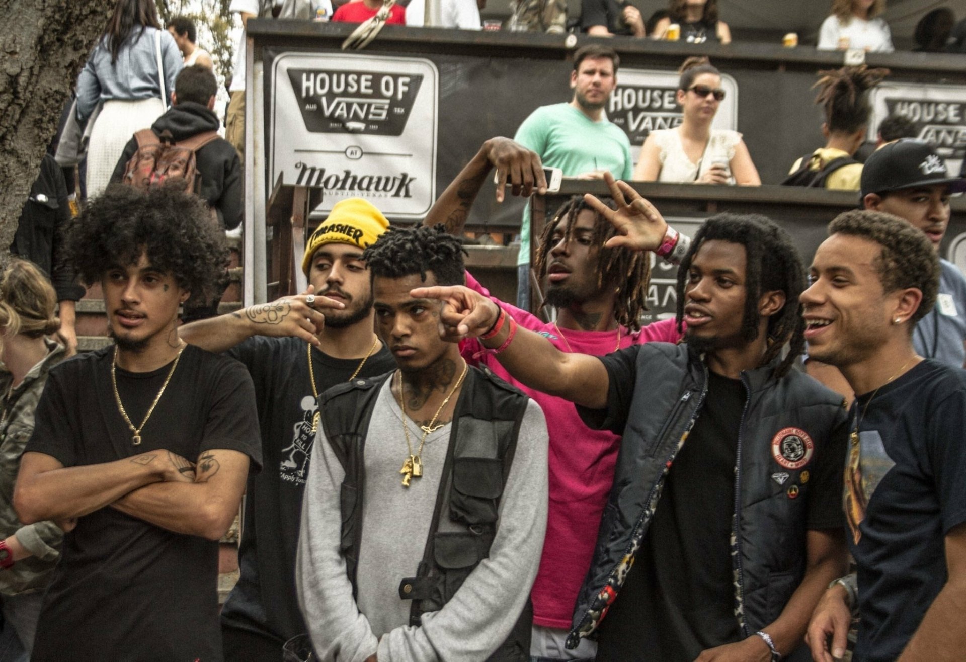 Group of young men posing together outdoors at a music event, with skateboarding and streetwear vibes.