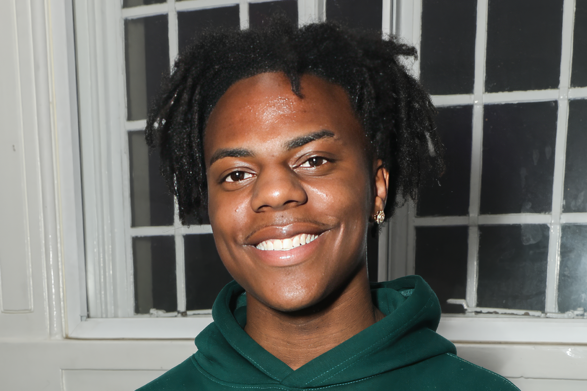 HD desktop wallpaper featuring a smiling individual with black dreadlocks wearing a green hoodie, tagged as IShowSpeed, against a window backdrop.