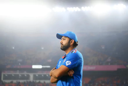 HD desktop wallpaper of a cricket player in blue jersey standing confidently on the field with stadium lights in the background.