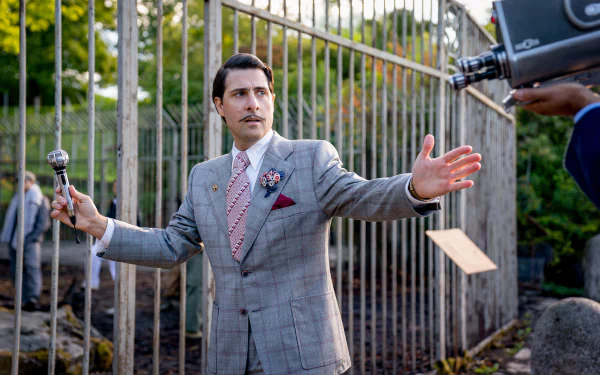 HD desktop wallpaper scene from The Hunger Games: The Ballad of Songbirds & Snakes showing a man in a suit addressing an off-camera crowd with a microphone, symbolizing a significant moment from the film.