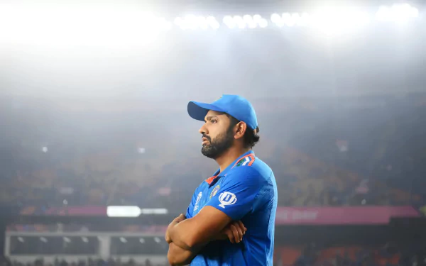 HD desktop wallpaper of a cricket player in blue jersey standing confidently on the field with stadium lights in the background.