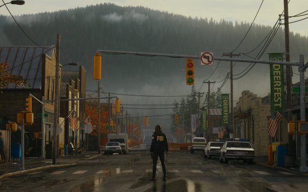 HD desktop wallpaper featuring Alan Wake 2 with a mysterious figure standing in the center of a foggy, small-town street, surrounded by forested hills in the background, setting a suspenseful scene.
