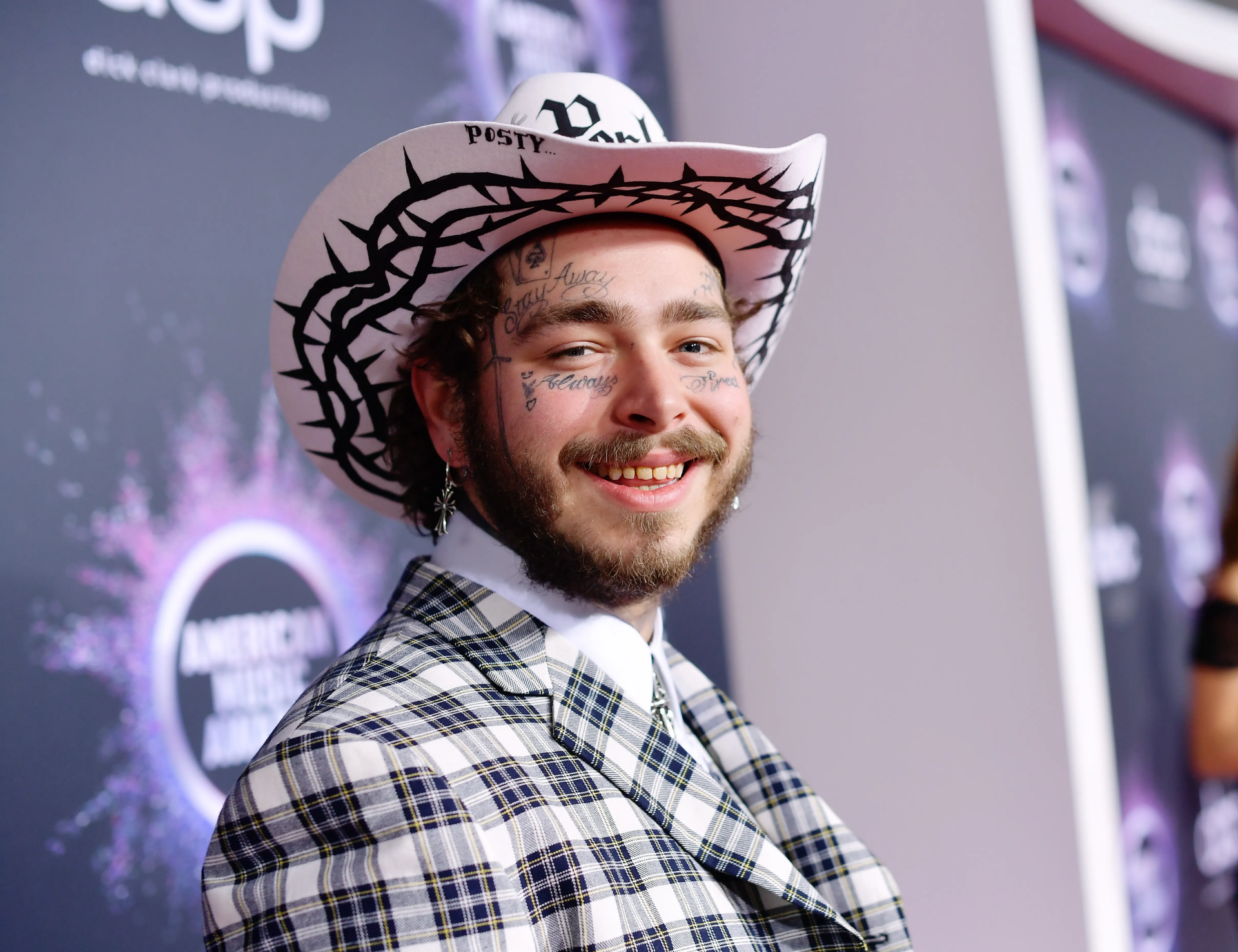 Smiling man in a white cowboy hat and plaid jacket at a red carpet event, HD desktop wallpaper background.