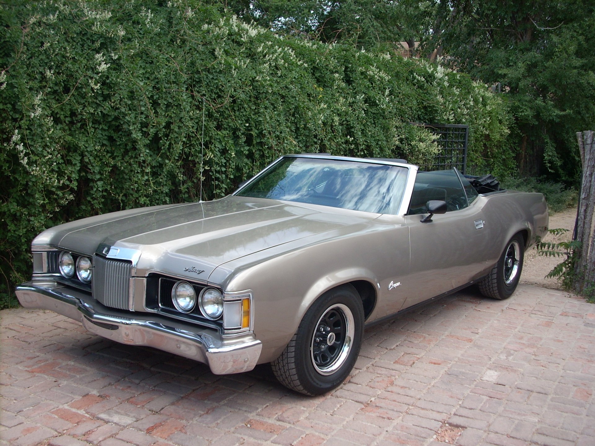 HD desktop wallpaper featuring a classic Mercury Cougar convertible parked on a brick driveway with lush greenery in the background.
