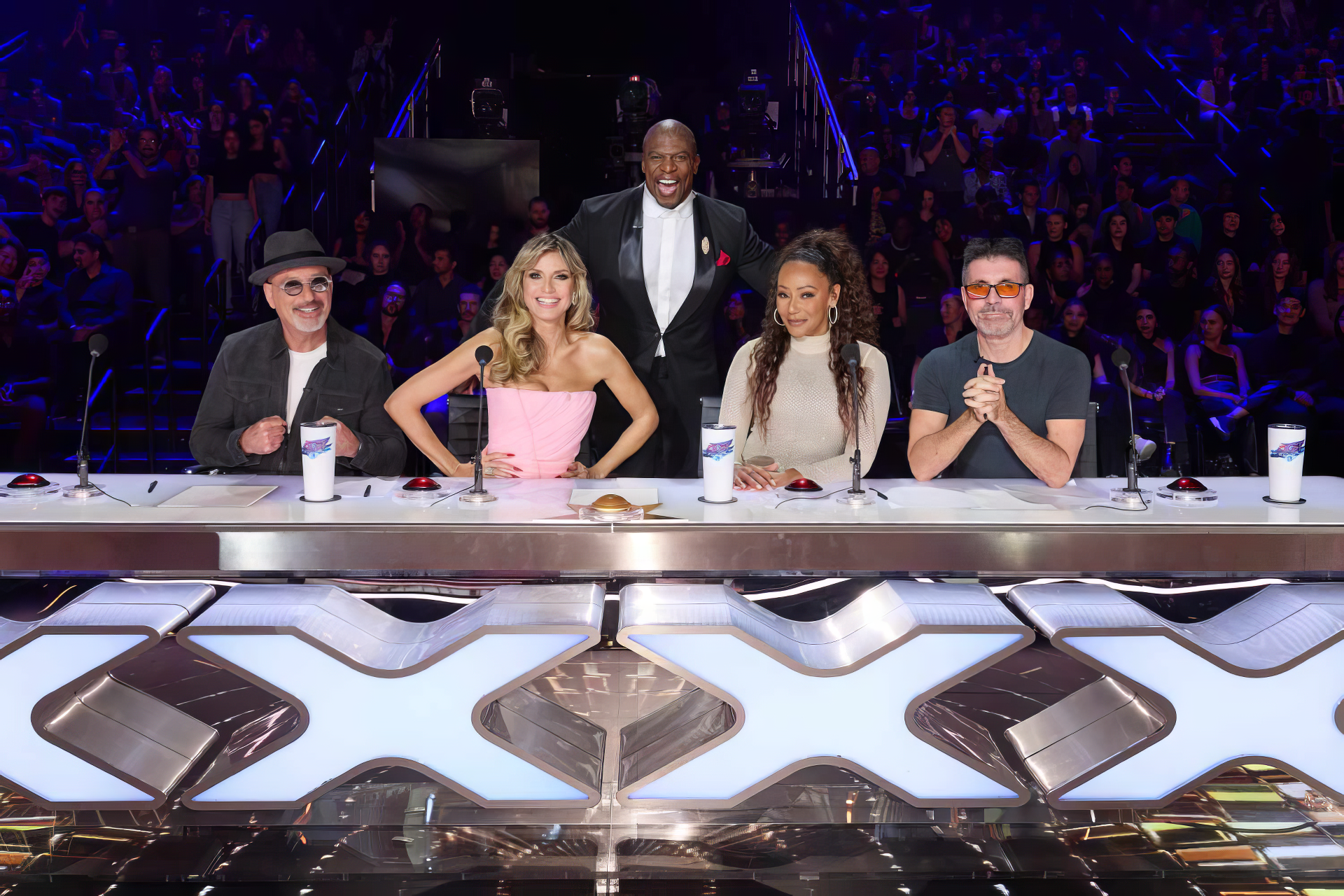 Judges panel of America's Got Talent with host standing behind in a vibrant HD desktop wallpaper capturing the excitement of the TV show.