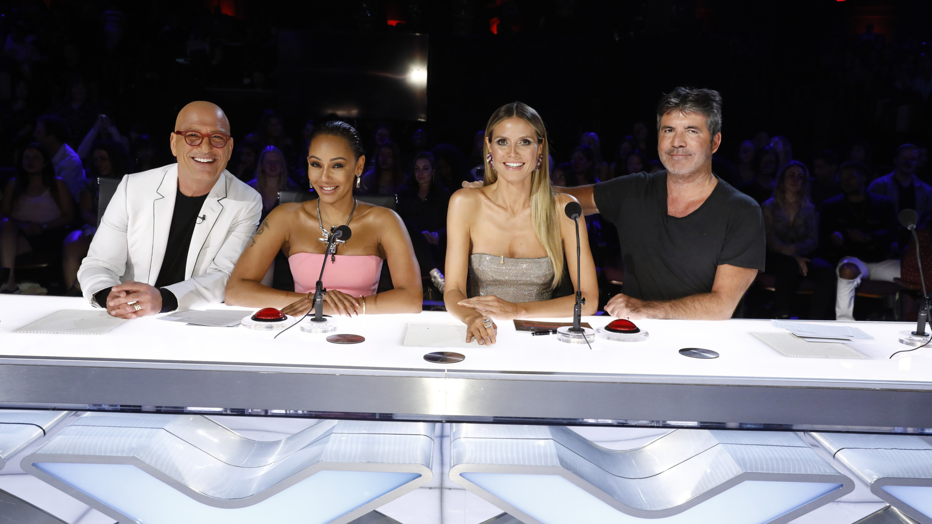 Judges panel from America's Got Talent TV show smiling at their desk for an HD desktop wallpaper background.