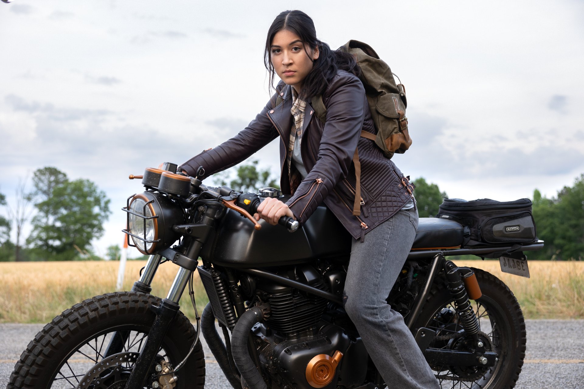 Alaqua Cox as Echo, confidently riding a motorcycle against a backdrop of open fields, featured in this HD desktop wallpaper from the TV show.
