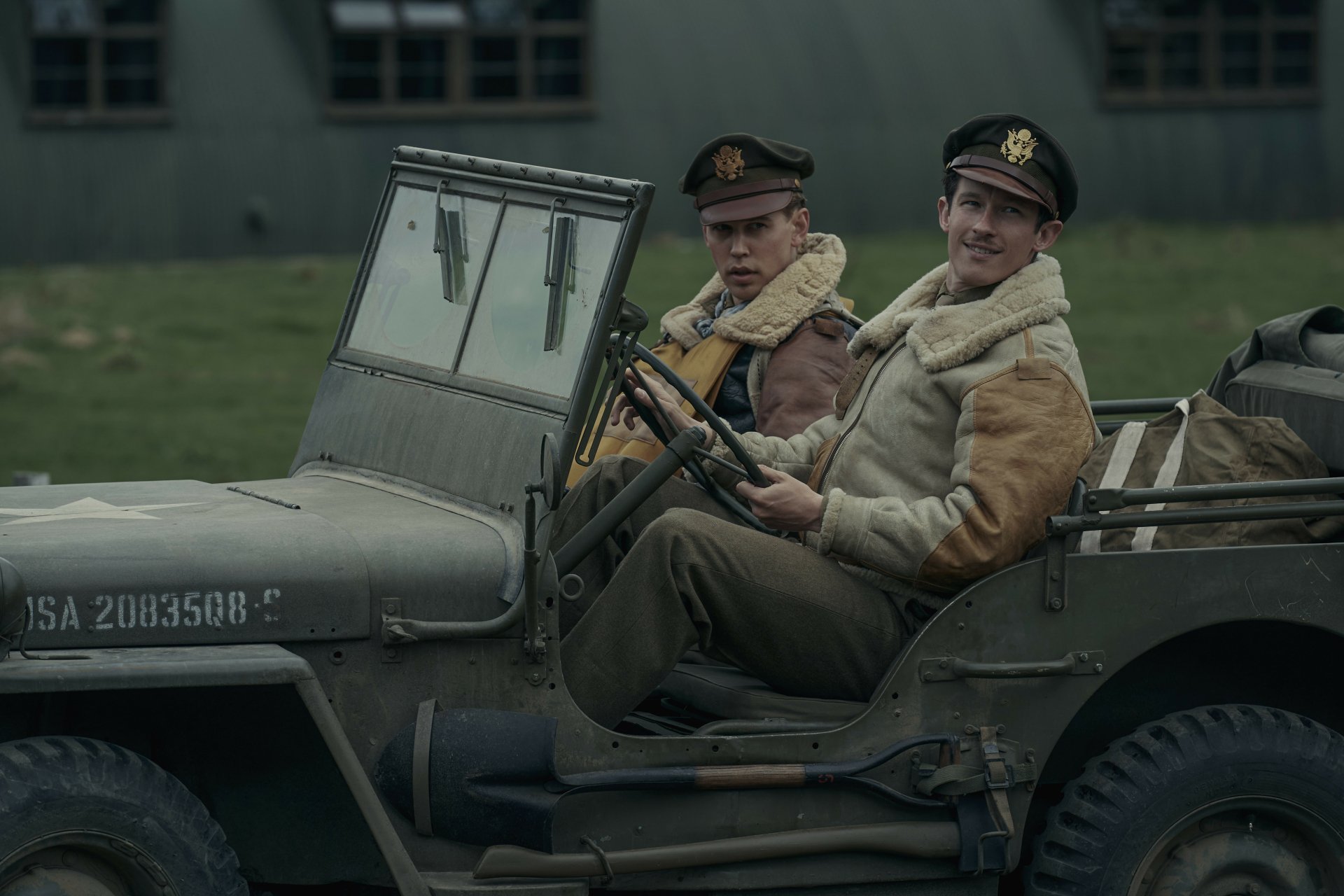 HD wallpaper featuring two characters from the TV show 'Masters of the Air' sitting in a vintage military jeep against a backdrop of wartime structures.