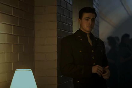 HD wallpaper featuring a scene from the TV show Masters of the Air, depicting a young man in a military uniform standing thoughtfully next to a lamp in a dimly lit hallway.