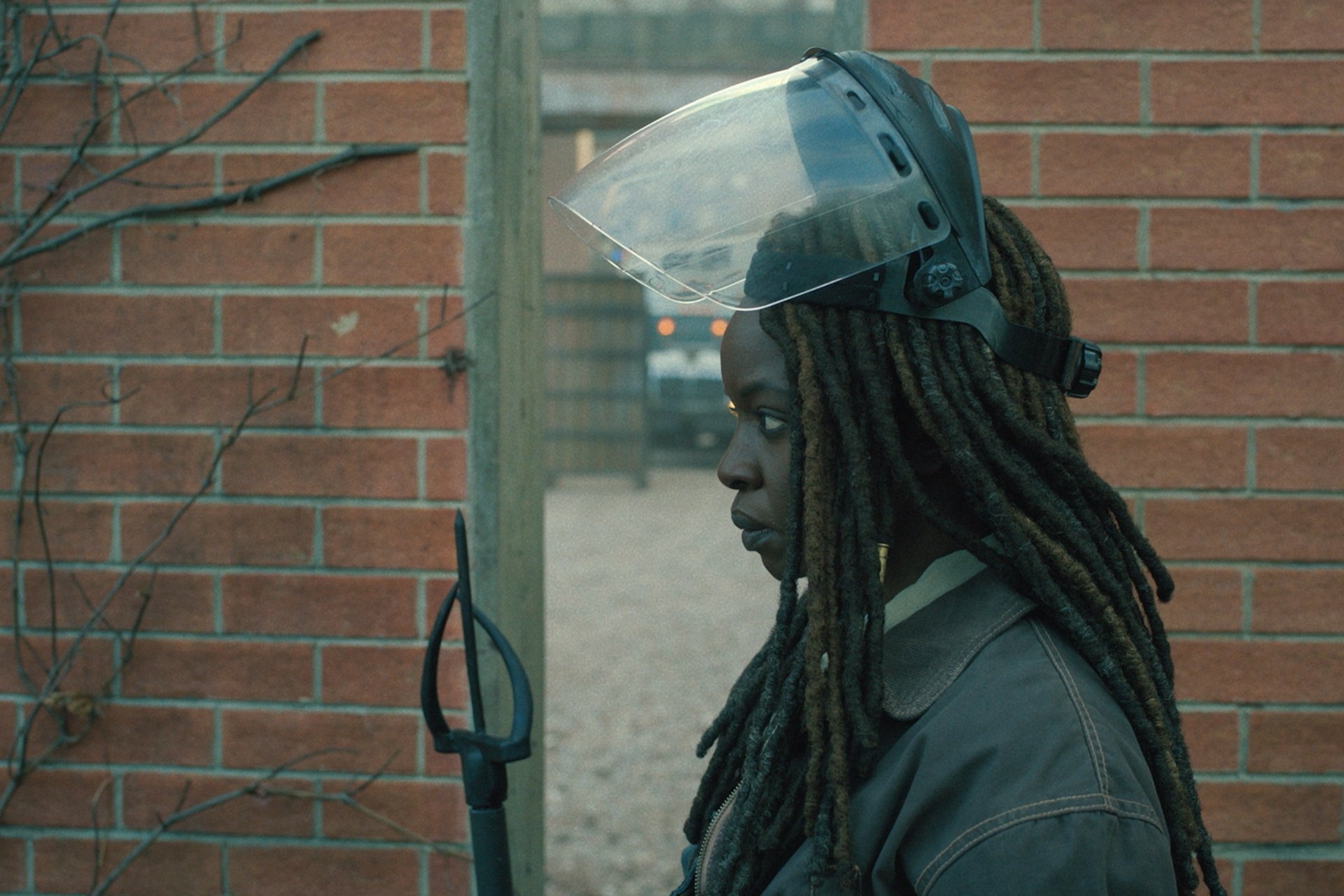 HD desktop wallpaper featuring a side profile of a character from the TV show The Walking Dead: The Ones Who Live, equipped with a protective headgear, set against a brick wall backdrop.