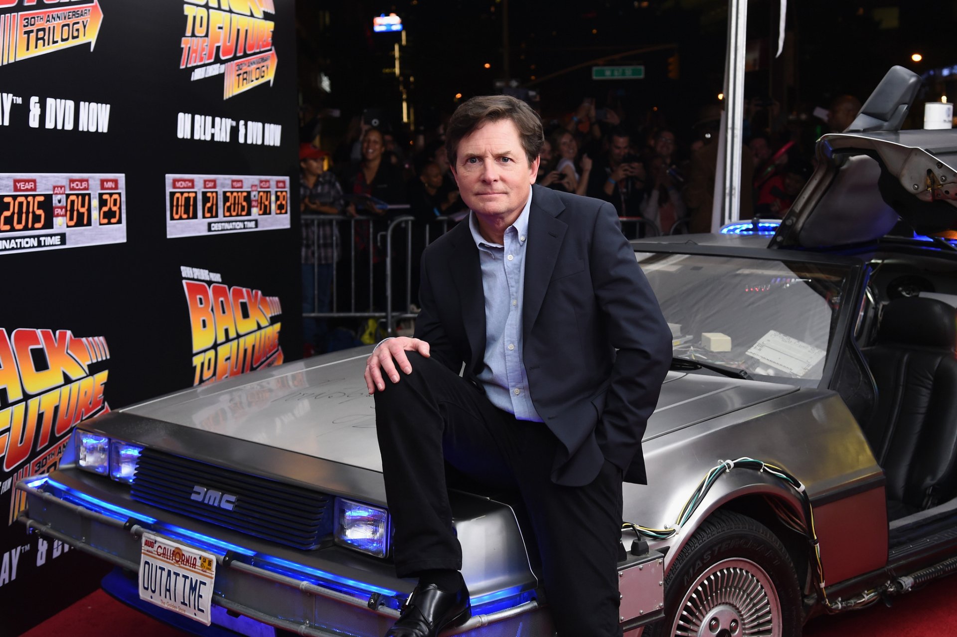 HD wallpaper of a person associated with Back To The Future leaning on a DeLorean, with movie branding in the background.