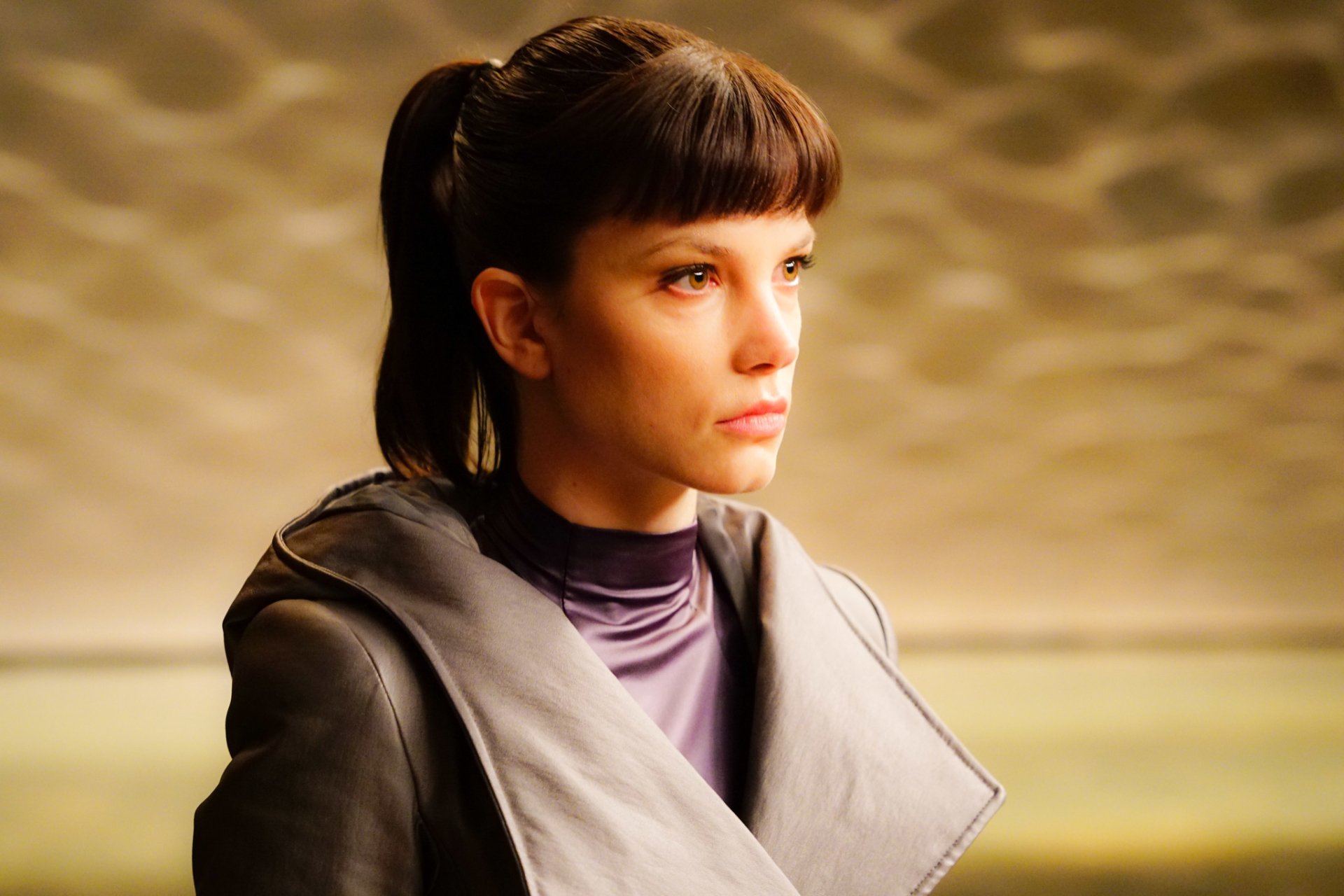 HD wallpaper featuring a character from movie Blade Runner 2049, with a focused expression and futuristic attire, against a textured background.