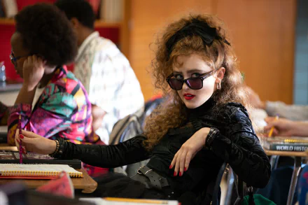 Stylish character from the movie Lisa Frankenstein sitting in a classroom, poised with sunglasses, portraying a bold and edgy look in a high-definition desktop wallpaper.