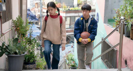 HD wallpaper from the movie Past Lives featuring two characters walking down outdoor stairs in a residential area.