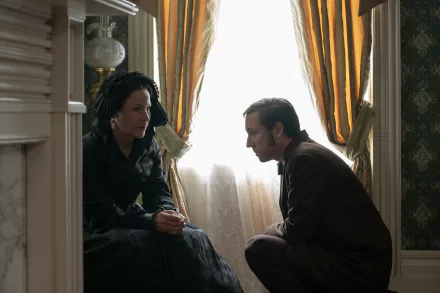 A tense moment between two characters in the TV show *Manhunt (2024)*, featuring a dimly lit room with elegant decor and soft sunlight filtering through the curtains.