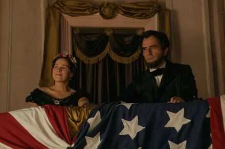 HD wallpaper featuring a scene from the TV show Manhunt (2024) with two actors behind an American flag, evoking a historical setting.