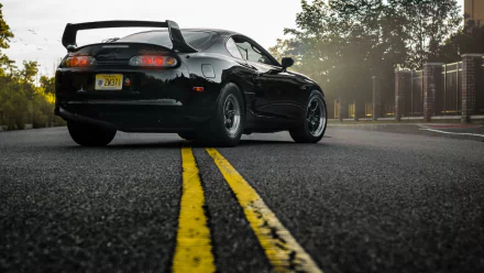 HD wallpaper of a black Toyota Supra parked on a road with a yellow dividing line, suitable as a desktop background.