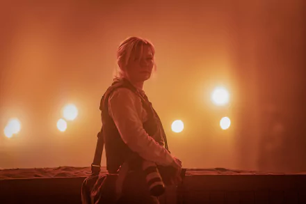 HD wallpaper featuring an individual resembling Kirsten Dunst from the side, set against a moody, amber-lit backdrop that creates a somber atmosphere, potentially from the movie Civil War (2024).