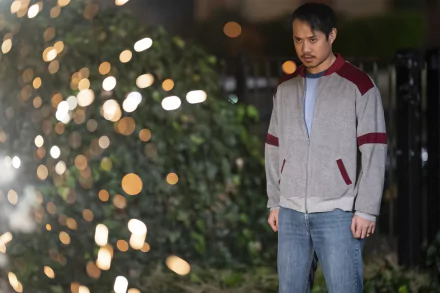 A man wearing a casual jacket stands in focus against a blurred background with sparkling lights, in a scene from the TV show The Sympathizer. The image is formatted as a high-definition desktop wallpaper.