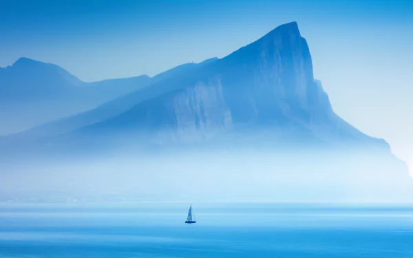 HD wallpaper featuring a serene catamaran sailing near a mist-covered island on a calm blue ocean.